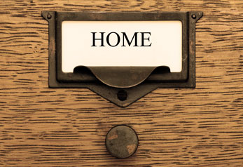Picture of the front of a small, vintage wooden drawer with a paper label in a metal encasing and a metal pull. Label shows the text HOME and links to the home page.